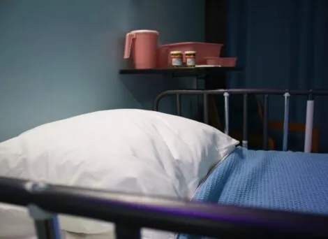 An empty hospital bed with table nearby illustrates Seaside healthcare Sun Behavioral Health deal